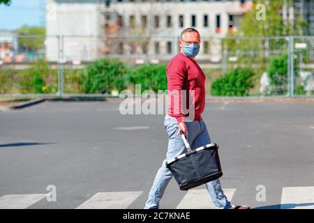 Homme avec la protection de bouche-nez en raison de la crise corona sur le chemin du supermarché avec un panier Banque D'Images