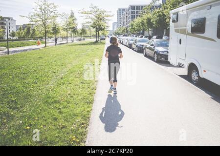 Vue arrière d'une jeune femme avec des écouteurs, elle prend son enrame à Munich, vit, vit et travaille dans la capitale bavaroise sur l'Isar. Banque D'Images