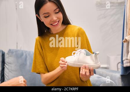 Belle fille asiatique souriante tenant la sneaker blanche entre les mains dans le magasin de mode Banque D'Images