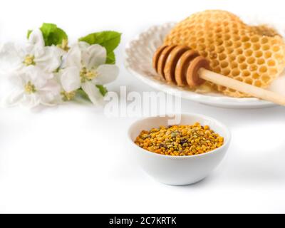 Grains de pollen d'abeille dans un bol en céramique blanc et rayons de miel sur fond blanc. Banque D'Images