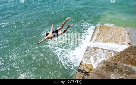 Brighton UK 18 juillet 2020 - UN jeune homme saute dans la mer d'une groyne sur la plage de Brighton lors d'une belle journée ensoleillée sur la côte sud avec des températures qui devraient atteindre les 20 hautes dans certaines parties de la Grande-Bretagne : Credit Simon Dack / Alay Live News Banque D'Images