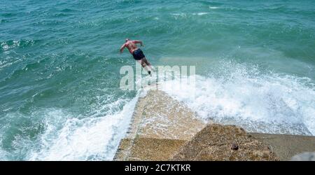 Brighton UK 18 juillet 2020 - UN jeune homme saute dans la mer d'une groyne sur la plage de Brighton lors d'une belle journée ensoleillée sur la côte sud avec des températures qui devraient atteindre les 20 hautes dans certaines parties de la Grande-Bretagne : Credit Simon Dack / Alay Live News Banque D'Images