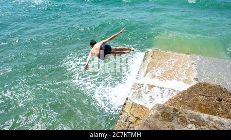 Brighton UK 18 juillet 2020 - UN jeune homme saute dans la mer d'une groyne sur la plage de Brighton lors d'une belle journée ensoleillée sur la côte sud avec des températures qui devraient atteindre les 20 hautes dans certaines parties de la Grande-Bretagne : Credit Simon Dack / Alay Live News Banque D'Images