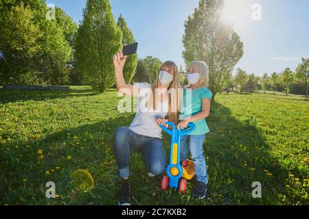 Mère et fille avec masque de visage font selfie dans un parc de ville, crise de Corona, Ratisbonne, Bavière, Allemagne Banque D'Images