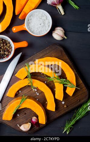 morceaux de citrouille crus sur une planche à découper avec romarin, sel, épices sur une table sombre ancienne. Légumes préparés pour cuire au four. Automne cuisine maison Banque D'Images