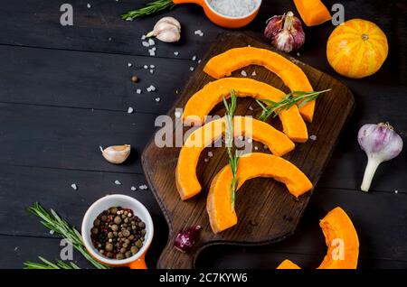 morceaux de citrouille crus sur une planche à découper avec romarin, sel, épices sur une table sombre ancienne. Légumes préparés pour cuire au four. Automne cuisine maison Banque D'Images