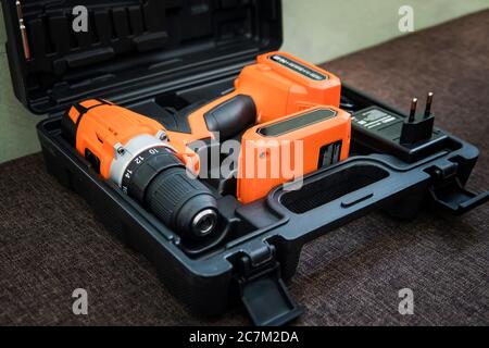 Perceuse sans fil orange avec batterie noire. Un tournevis orange ou une perceuse dans un conteneur noir repose sur le sol. Outil de serrage des vis. Pistolet à vis Banque D'Images