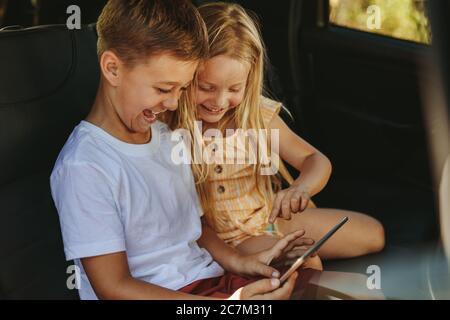 Deux enfants assis sur la banquette arrière de la voiture jouant à des jeux sur une tablette numérique. voyager en voiture. Banque D'Images