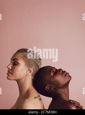Vue latérale de deux femmes différentes les unes contre les autres sur fond beige avec espace de copie. Modèles féminins de différentes origines ethniques debout dos à dos an Banque D'Images