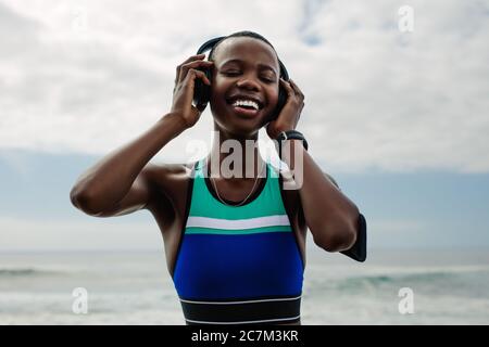 Femme souriante avec casque écoutant de la musique pendant une pause d'entraînement. Femme qui écoute de la musique après une séance d'entraînement en plein air. Banque D'Images