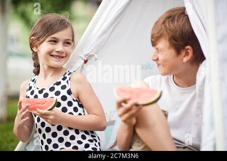 De jolis petits enfants dans la cour en tipi et mange de la pastèque. Banque D'Images