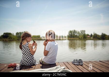 Des enfants souriants sur du bois près de l'étang en train de manger de la pastèque fraîche. Banque D'Images