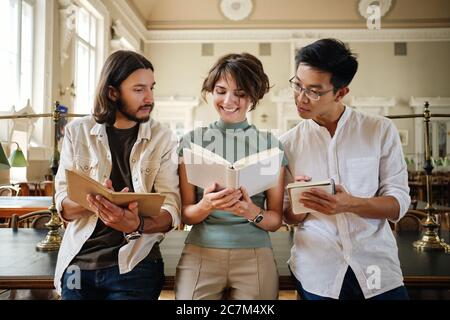 Groupe de jeunes étudiants multinationaux occasionnels heureux d'étudier avec le livre ensemble dans la bibliothèque de l'université Banque D'Images