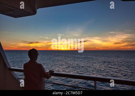 Une femme au train du bateau de croisière en silhouette regarde un beau coucher de soleil descendre au-dessus de la mer Banque D'Images