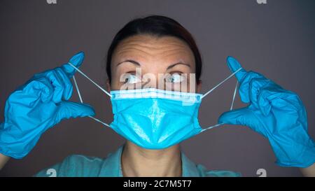 Une femme médecin ou infirmière avec des gants en caoutchouc sur ses mains met un masque bleu sur son visage. Banque D'Images