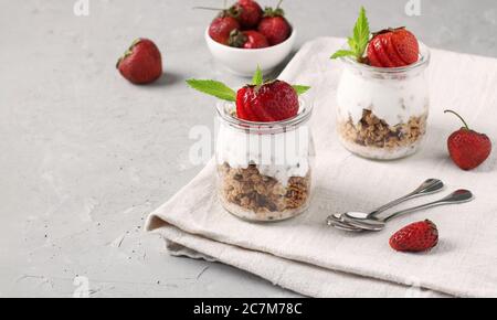 Muesli au miel croustillant de granola avec fraise et yaourt naturel, délicieux et sain petit déjeuner dans des pots en verre sur fond gris Banque D'Images