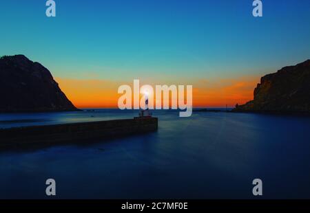 Belle scène d'un phare à faro dans un port dans un ciel bleu-orange avec une montagne rocheuse Banque D'Images