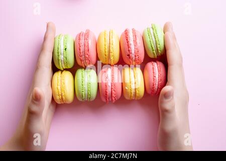 Fille tenant dix macarons français colorés entre les mains, vue du dessus Banque D'Images