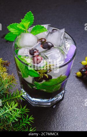 cocktail de baies, menthe, glace dans un verre rox sur une table noire vue bot, gros plan, orientation verticale Banque D'Images