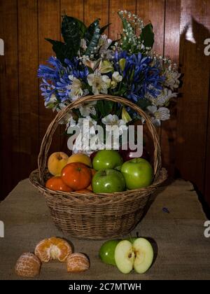 Panier rempli de mandarines, de pommes et de pêches sur la table avec un bouquet sur le fond Banque D'Images