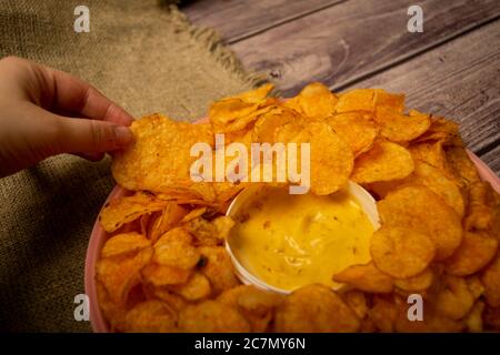 La fille prend une puce dans un plat rond avec des chips de pomme de terre et une casserole avec sauce au fromage au centre de l'assiette. Gros plan Banque D'Images