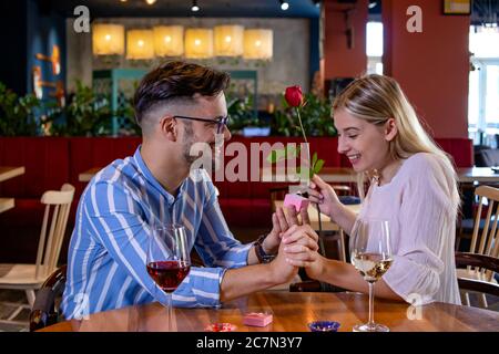 Jeune couple romantique dans un magnifique restaurant chic. Petit ami surprenez sa petite amie avec une rose rouge et proposez-lui avec un anneau d'engagement. Banque D'Images