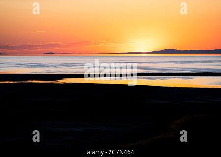 Coucher de soleil sur le Grand Lac salé dans le parc national d'Antelope Island avec surface d'eau et silhouette de plage près du lac Ladyfinger Banque D'Images