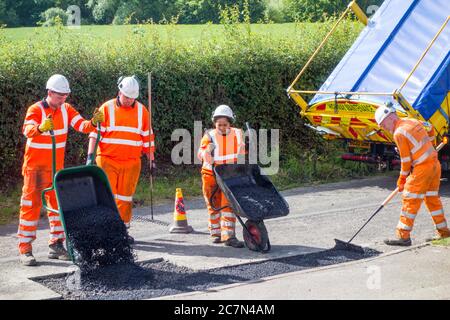 Ouvriers et femme effectuant des réparations de route réparer une surface de route inégale endommagée et des trous de pot avec le tarmac dans une route de campagne de Cheshire Angleterre Royaume-Uni Banque D'Images