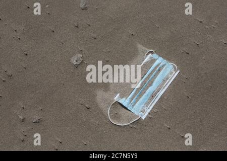 Un masque chirurgical jetable dans le sable sur une plage. Banque D'Images