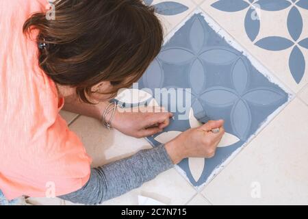 Séjour à la maison et amélioration de la maison concept: Jeune femme caucasienne avec T-shirt orange est de peindre les carreaux de sa maison. Banque D'Images