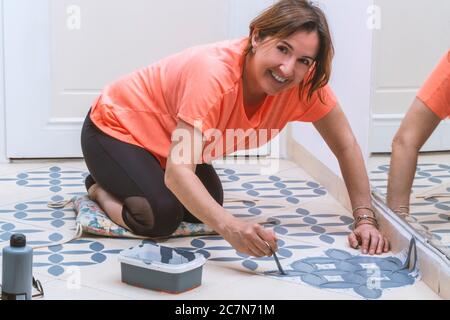 Séjour à la maison et amélioration de la maison concept: Jeune femme caucasienne avec T-shirt orange est de peindre les carreaux de sa maison. Banque D'Images