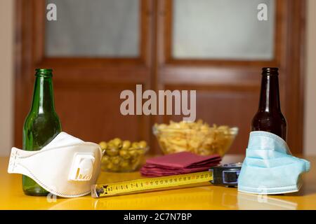 Bouteilles de bière recouvertes de masques médicaux à côté des olives, des chips et du ruban à mesurer sur la table Banque D'Images