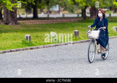 Kyoto, Japon - 17 avril 2019: Japonaise personne femme sur vélo vélo sur la rue Candid vie de ville à Kyoto Gyoen portant un masque Banque D'Images