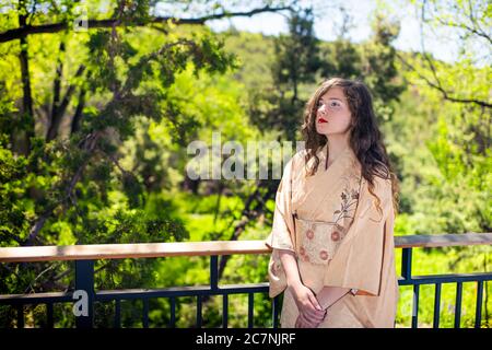 Jeune femme caucasienne vêtue en costume kimono par clôture de garde-corps dans le jardin extérieur zen maison Banque D'Images