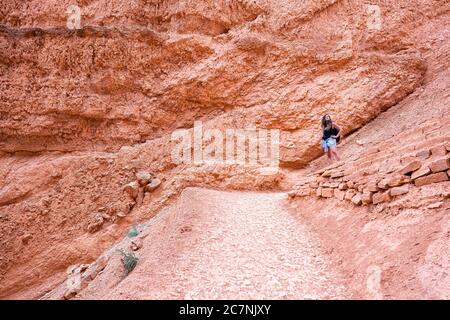 Femme debout à côté de formations de couleur rouge au Queens Garden Navajo Loop Trail au parc national de Bryce Canyon dans l'Utah avec caméra regardant de ste Banque D'Images