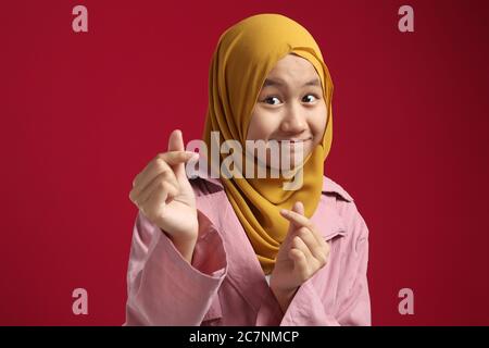 Portrait de la jeune fille musulmane asiatique souriante et du signe de l'amour, gros plan sur fond rouge Banque D'Images