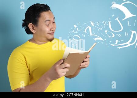 Portrait d'homme asiatique portant une chemise jaune décontractée semblait heureux et souriant en lisant un livre, lettres volantes avant le livre Banque D'Images