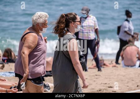 Barcelone, Espagne. 18 juillet 2020. Les personnes portant des masques sanitaires se promondent le long de la plage.la ville de Barcelone fait face à de nouvelles épidémies de cas de coronavirus avec de nouvelles restrictions de mobilité et recommandations pour éviter de voyager en dehors de la ville. Crédit : SOPA Images Limited/Alamy Live News Banque D'Images