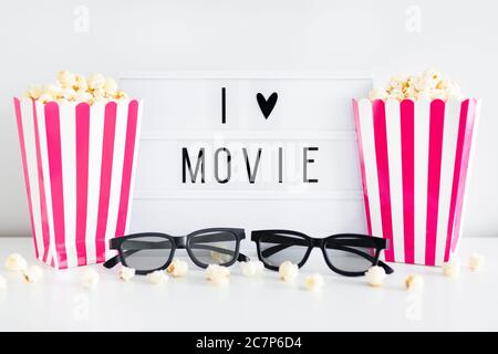 Cinema concept - boîtes à rayures rouges avec pop-corn, lunettes 3d et boîte lumineuse avec texte « I love movie » Banque D'Images