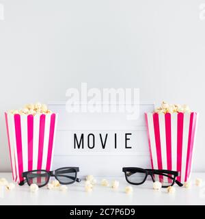 cinéma et concept de date - deux boîtes à rayures rouges avec pop-corn, lunettes 3d et boîte lumineuse avec mot de film Banque D'Images