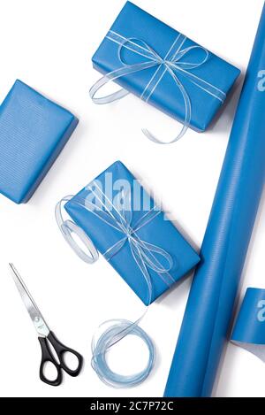 Boîtes-cadeaux emballées dans du papier bleu et le contenu d'un espace de travail composé sur fond blanc. Concept de décoration de fête et d'emballage cadeau. Idées de bricolage. Pose à plat Banque D'Images