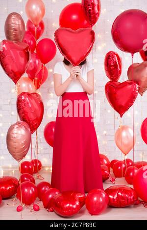 concept de la saint-valentin - portrait complet de la femme couvrant son visage avec un ballon rouge en forme de coeur Banque D'Images