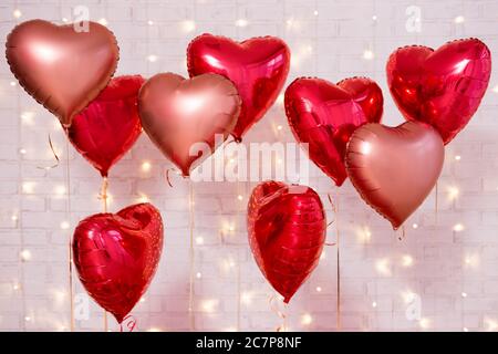 Arrière-plan de la Saint-Valentin - groupe de ballons rouges en forme de coeur sur le mur de brique blanche Banque D'Images