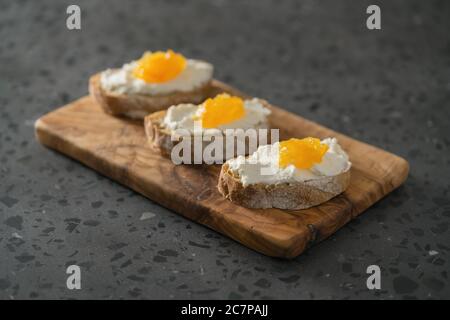 Trois tranches de ciabatta avec ricotta et marmelade d'orange sur l'olive bois sur surface de terrazzo Banque D'Images