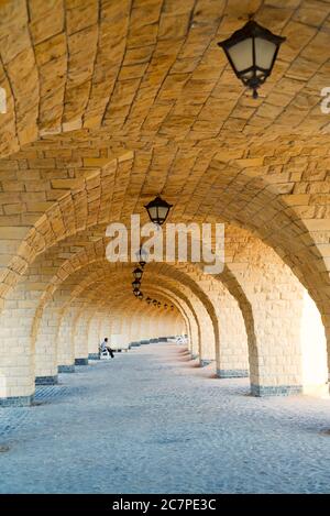 Vue architecturale ancienne depuis le couloir en briques voûtées avec des arcs et des colonnes de style arabe avec des lampes à l'ancienne au plafond. Banque D'Images