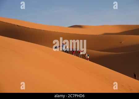 Touristes grimpant sur les dunes du désert du Sahara sous la lumière du jour. Près du village de Merzouga au Maroc Banque D'Images