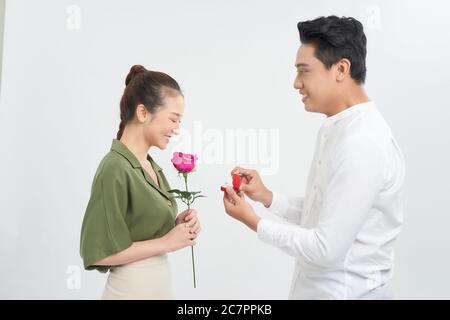 Une jeune femme attrayante est debout avec des roses dans les mains tandis que l'homme beau fait la proposition avec l'anneau dans les mains. Banque D'Images