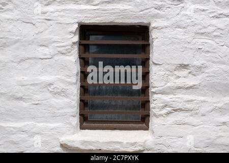 Fenêtre peinte en marron avec barres de sécurité sur un mur en pierre blanche, architecture d'île grecque, espace de copie. Modèle de carte vacances en Grèce Banque D'Images