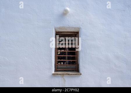 Fenêtre peinte en marron avec barres de sécurité sur un mur en pierre blanche, architecture d'île grecque, espace de copie. Modèle de carte vacances en Grèce Banque D'Images