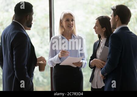 Les jeunes employés multiethniques écoutent les conseils de la femme d'âge moyen patron Banque D'Images